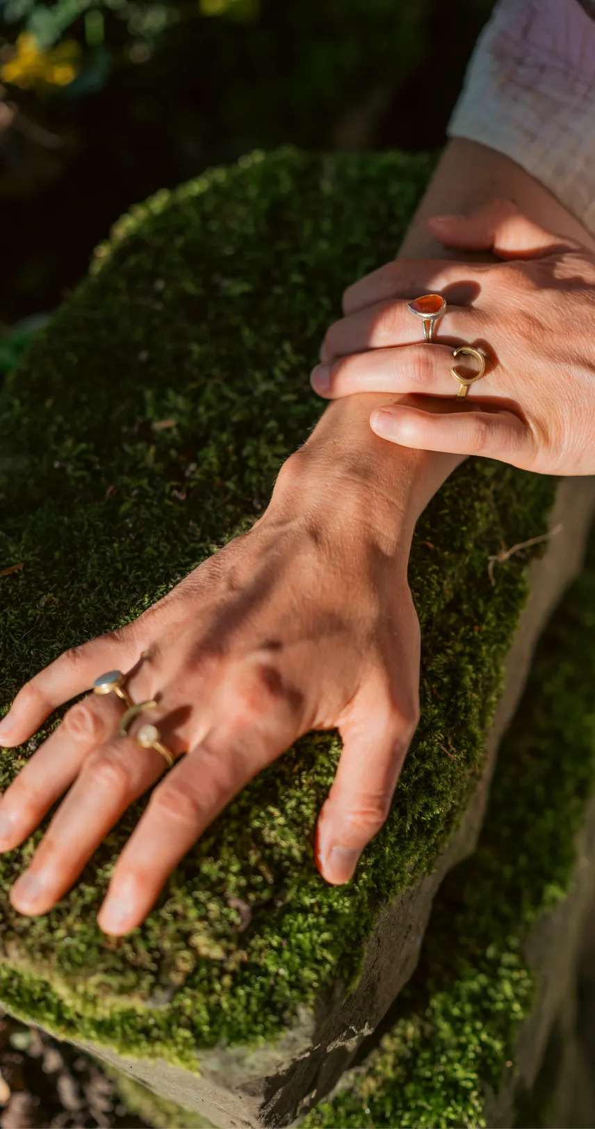 Eine Hand mit Ringen ruht auf bemoostem Boden